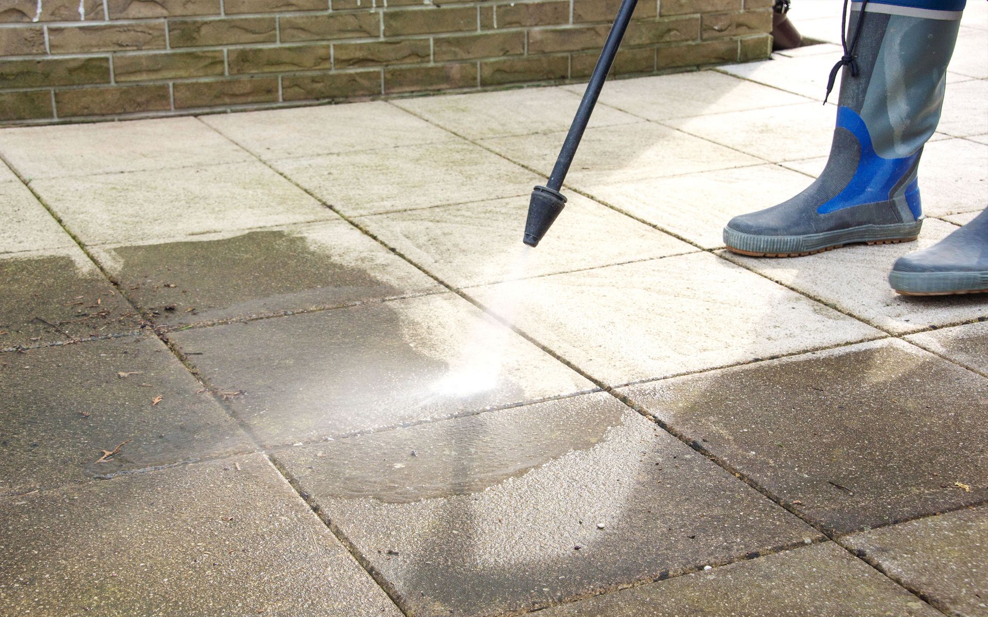 A person is using a high pressure washer to clean a tiled floor.