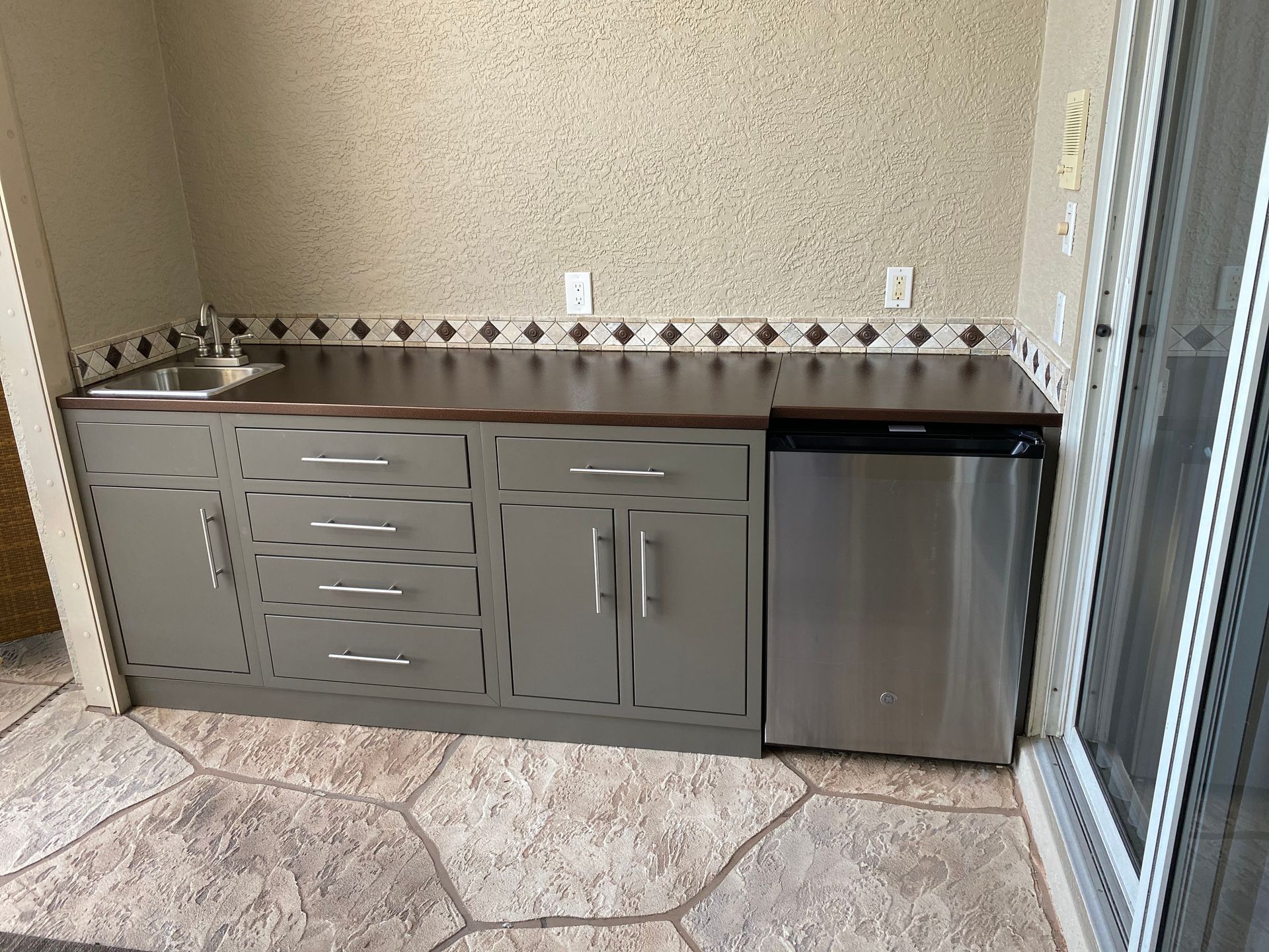 Outdoor kitchen with gray cabinets, stainless steel fridge, sink, and patterned backsplash