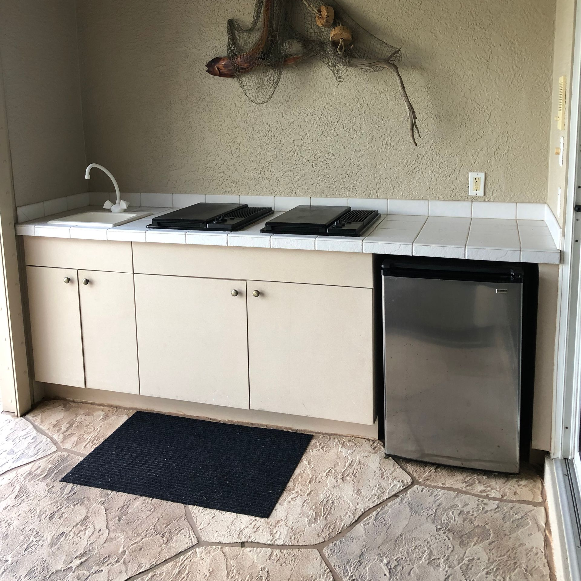 Outdoor kitchen with a sink, countertop, cabinets, a mini-fridge, and two flat top grills.