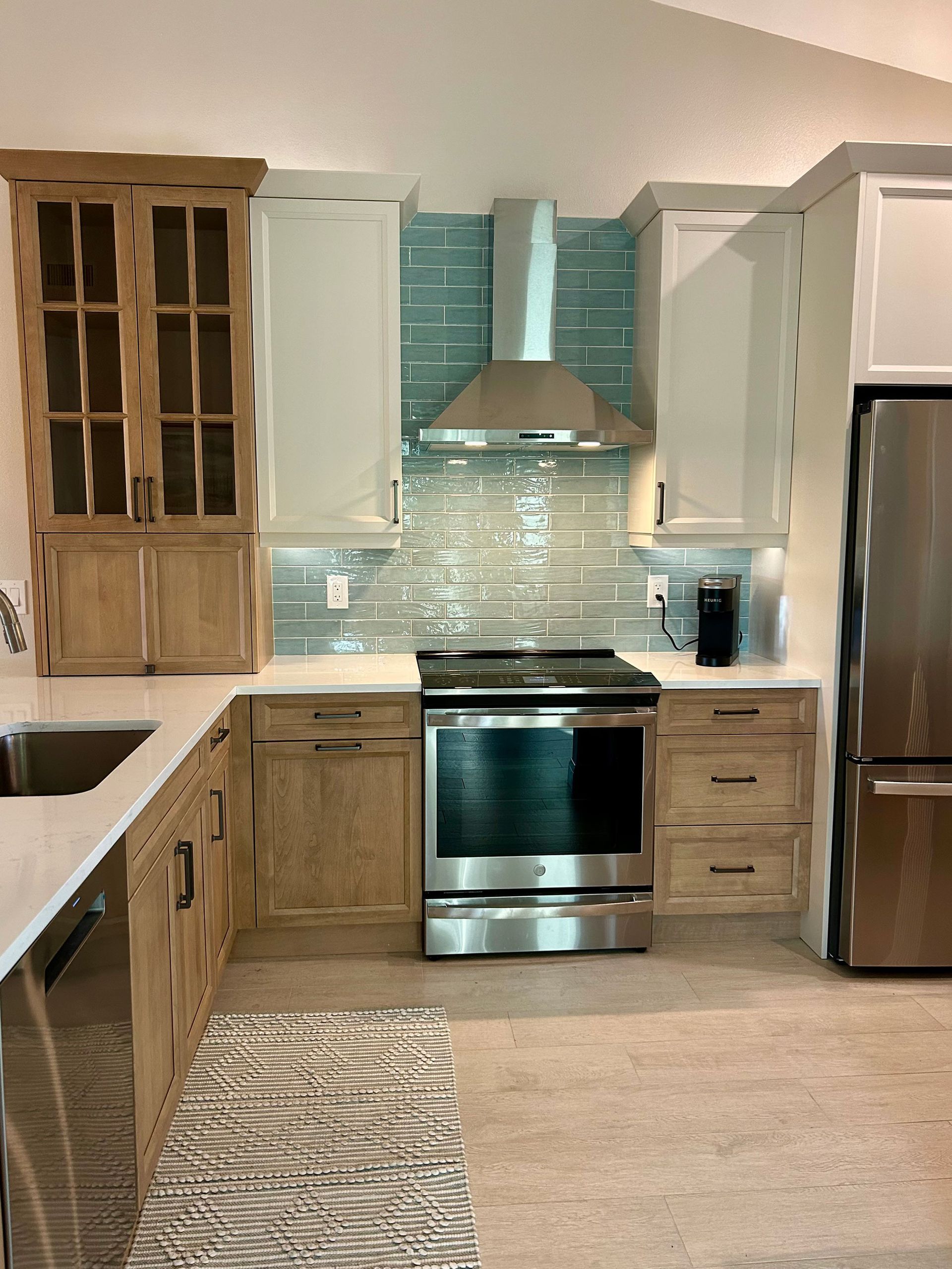 Kitchen with light wood and white cabinets, stainless steel appliances, and a blue tile backsplash.