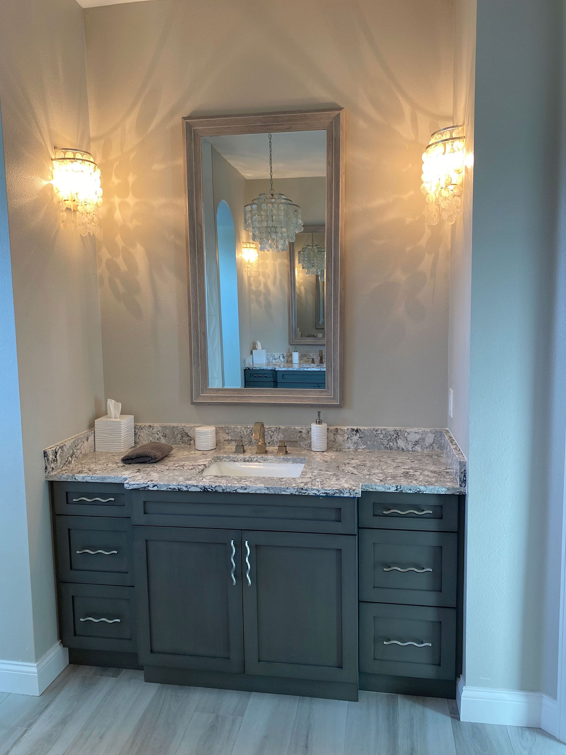 Bathroom with dark teal cabinets, granite countertop, mirror, and sconces.