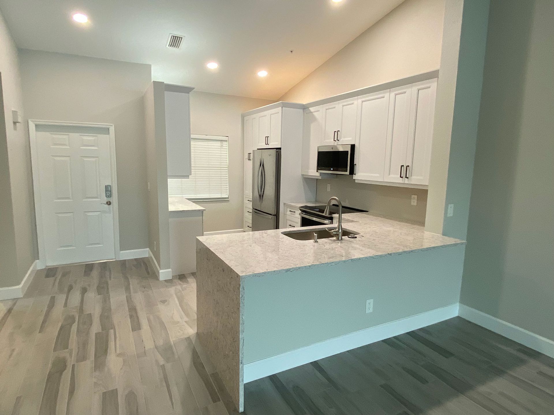 Bright kitchen with white cabinets, granite countertop, stainless steel appliances, and gray-toned wood flooring.