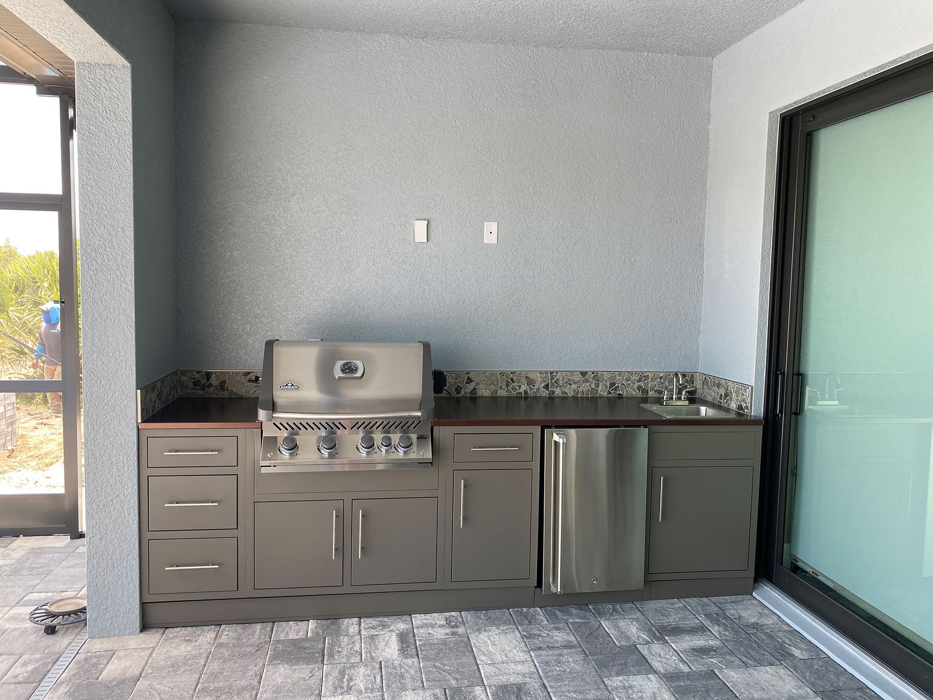 Outdoor kitchen with stainless steel grill, cabinets, and sink; neutral colors.