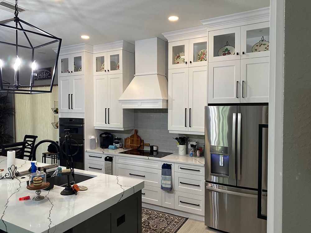 White kitchen with tall cabinets, stainless steel appliances, and a marble countertop island.