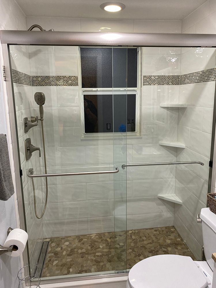 A modern shower with glass doors, white tile walls, and a pebble floor.