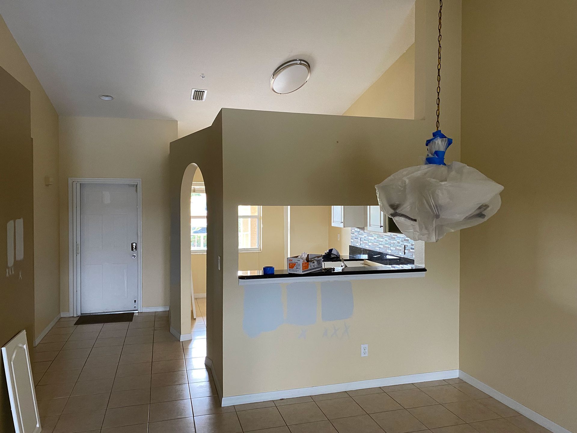 Interior with doorway, archway, and partial wall opening to a kitchen. Light yellow walls and a hanging light fixture.