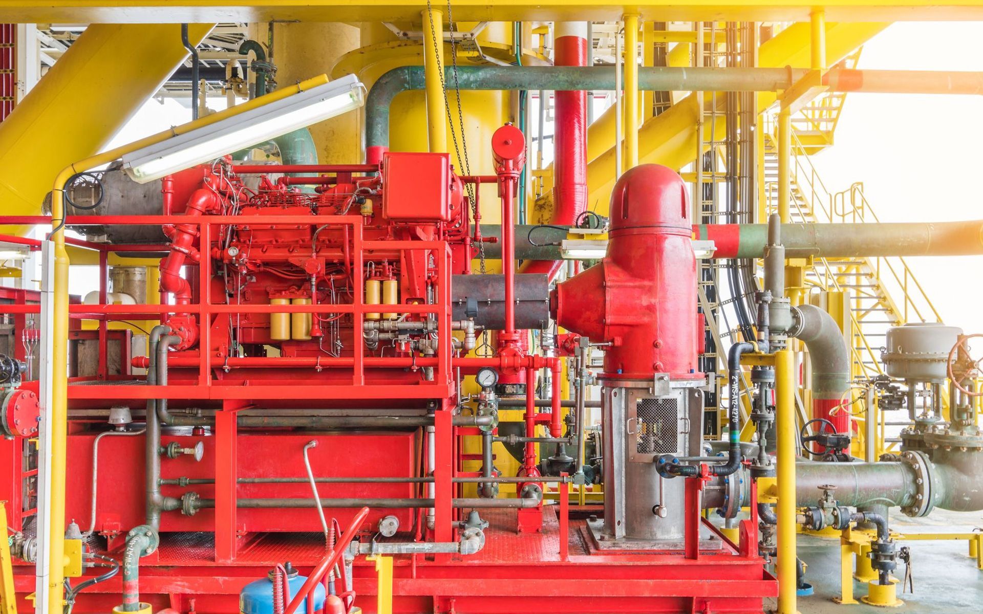 An industrial fire pump engine painted bright red is installed on an offshore oil platform with yellow piping.