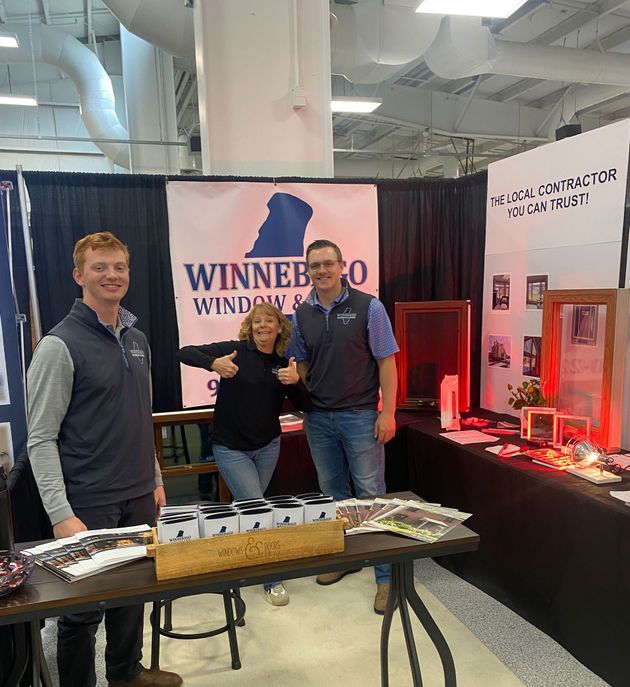 Three people at a trade show booth with a Winnebago banner and display tables