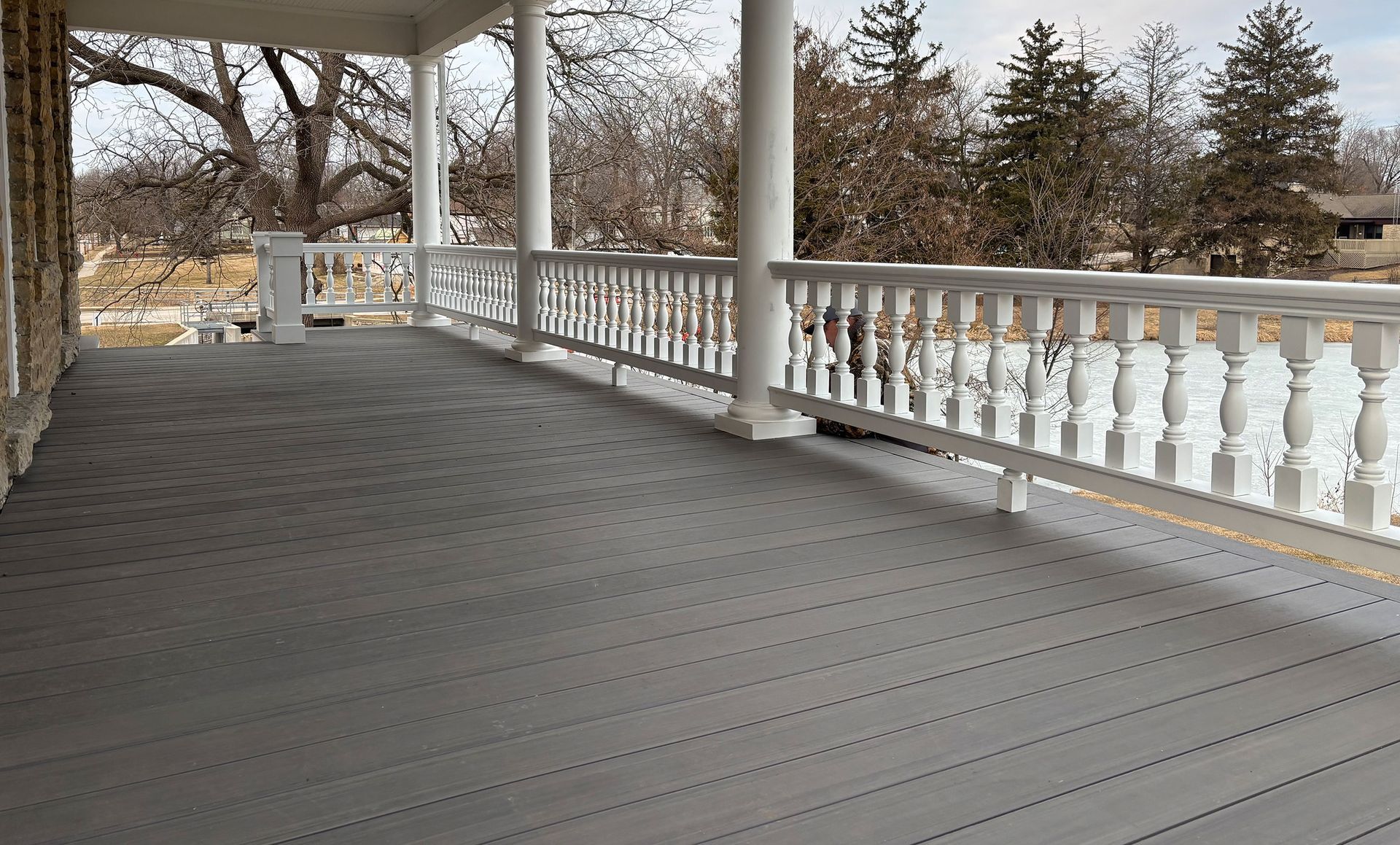 Covered porch with gray deck and white railing overlooking a yard