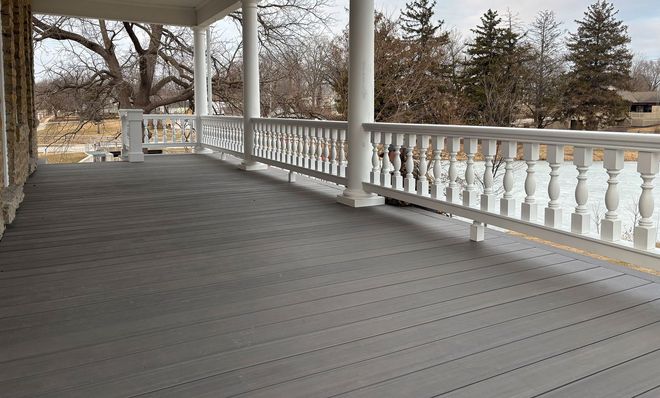 Covered porch with gray deck and white railing overlooking a yard