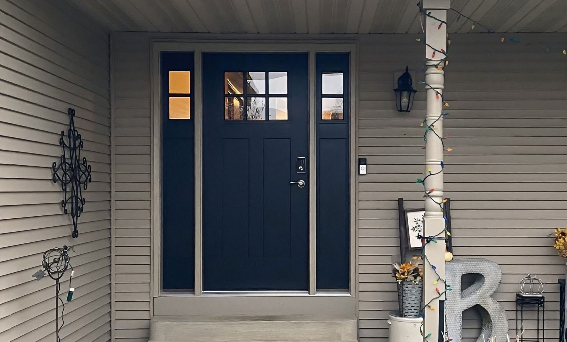 Front porch with blue double doors, beige siding, and a lit wall lantern.