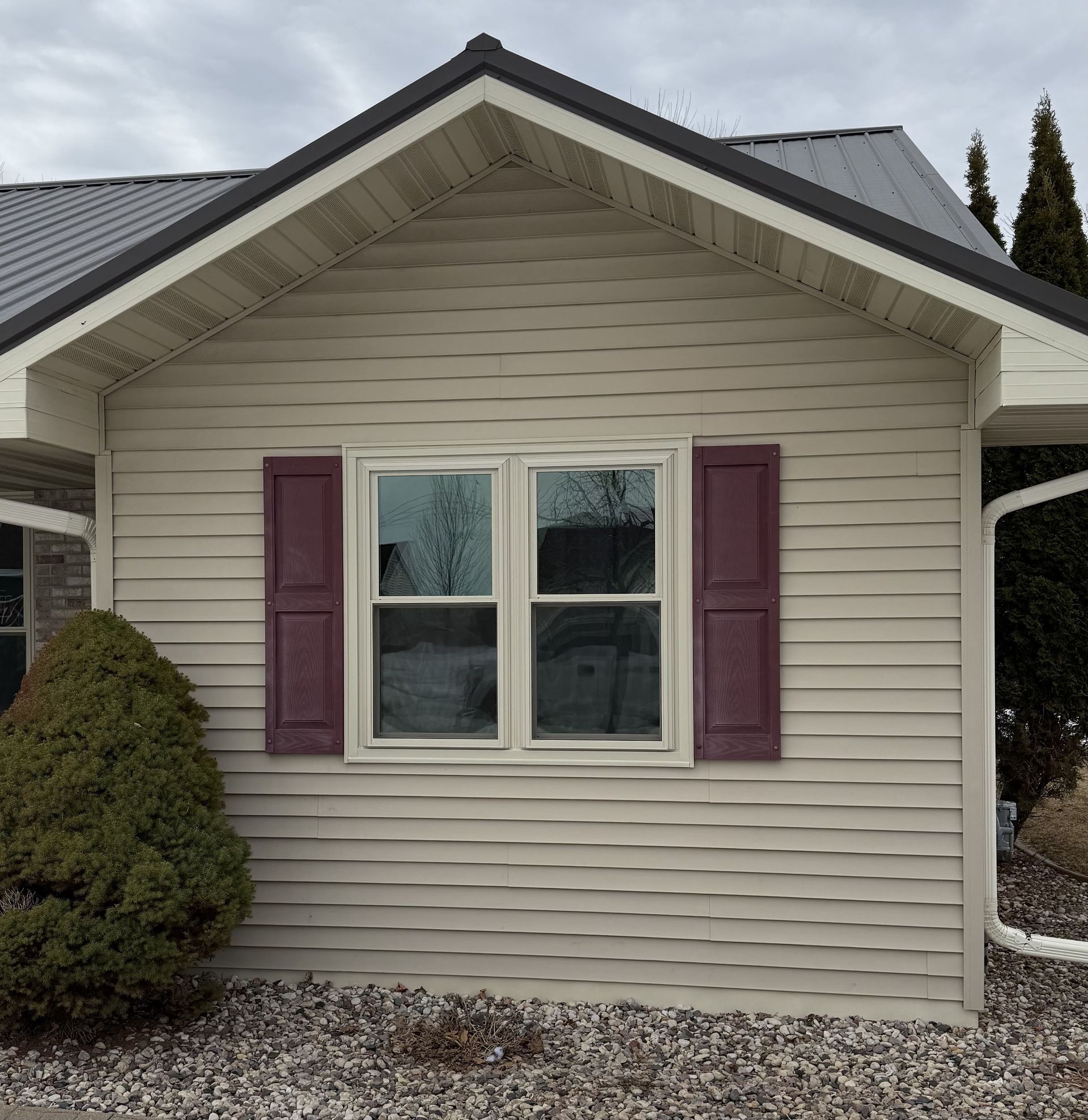 Small beige house facade with a white-trim window and purple shutters under a gabled roof.