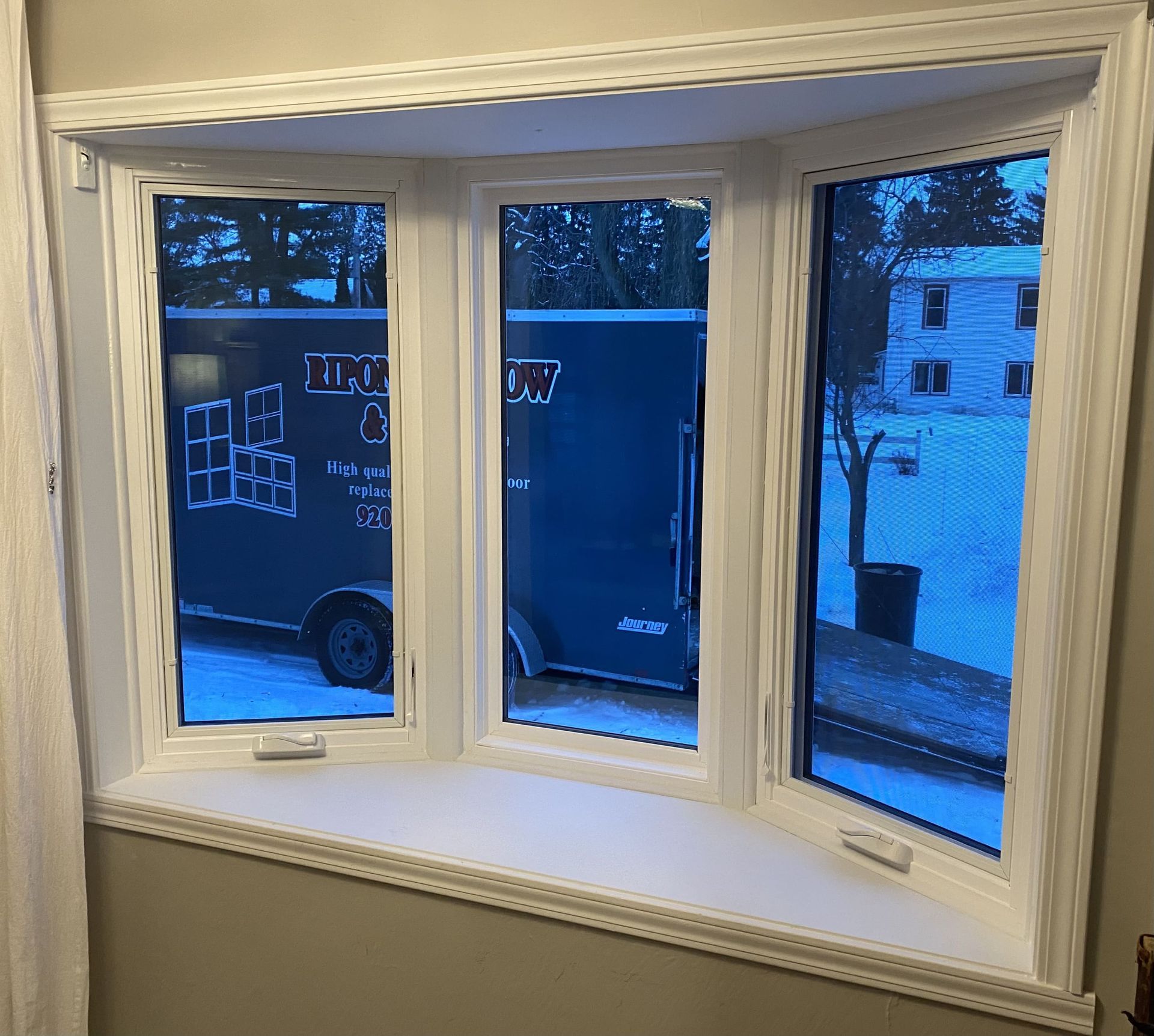 Bay window with white trim overlooking a dark blue delivery truck on a snowy street