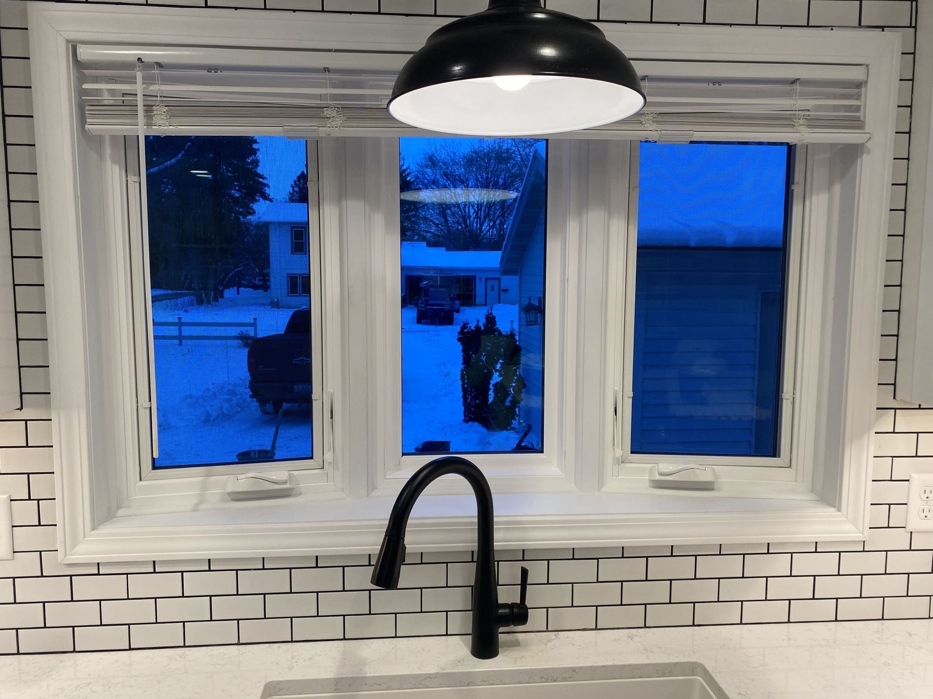 Kitchen window with white trim, blue evening light outside, and a black faucet below a hanging pendant lamp