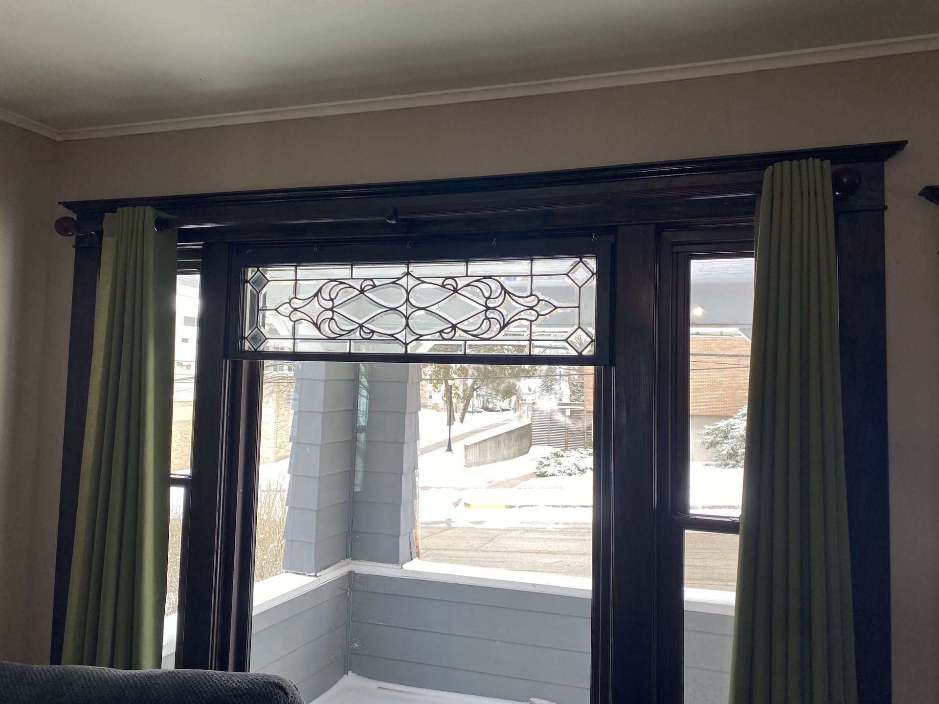 Window with green curtains overlooking a snowy street and neighboring houses