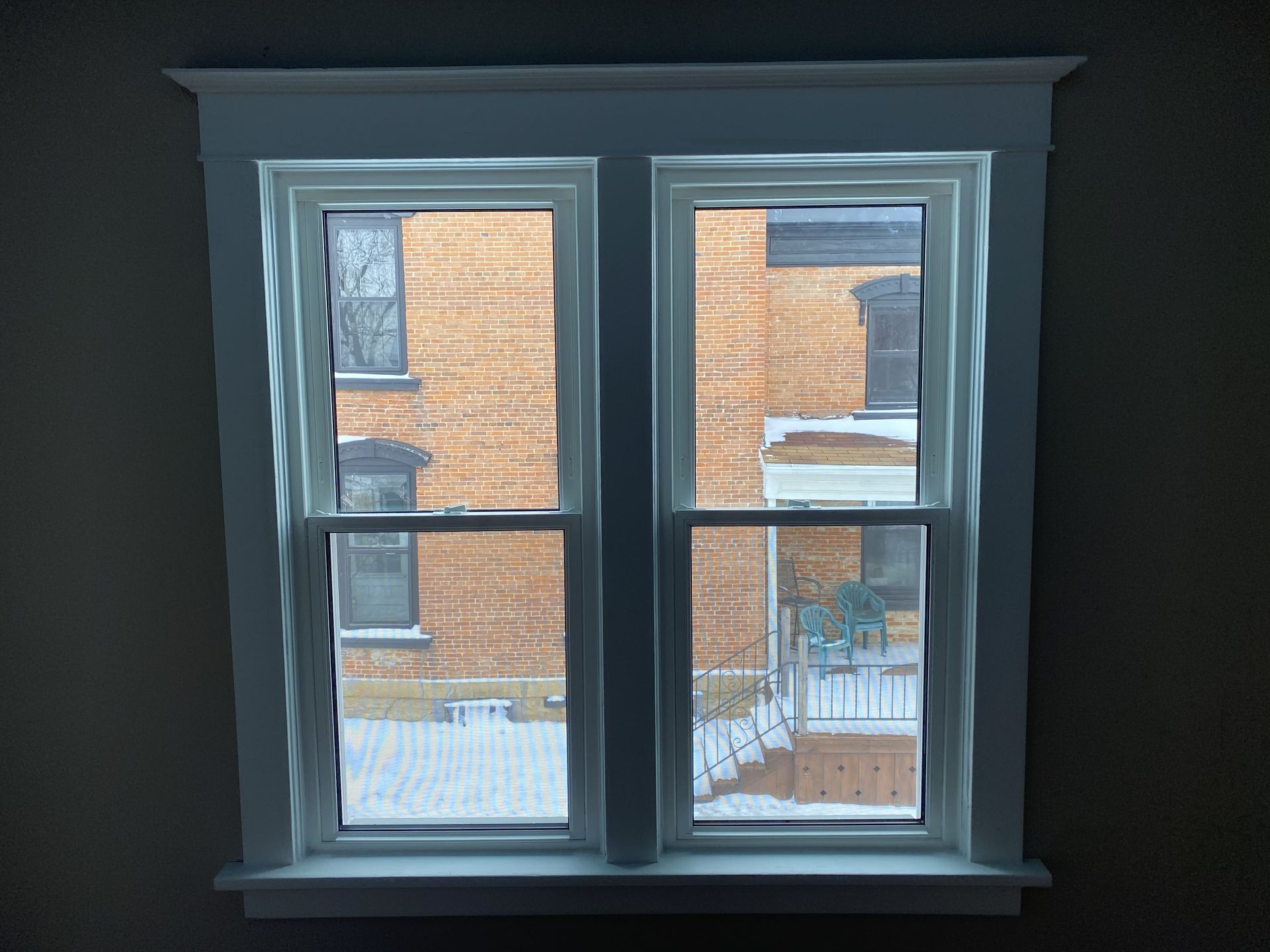 Two white-framed windows overlooking a snowy brick building exterior.