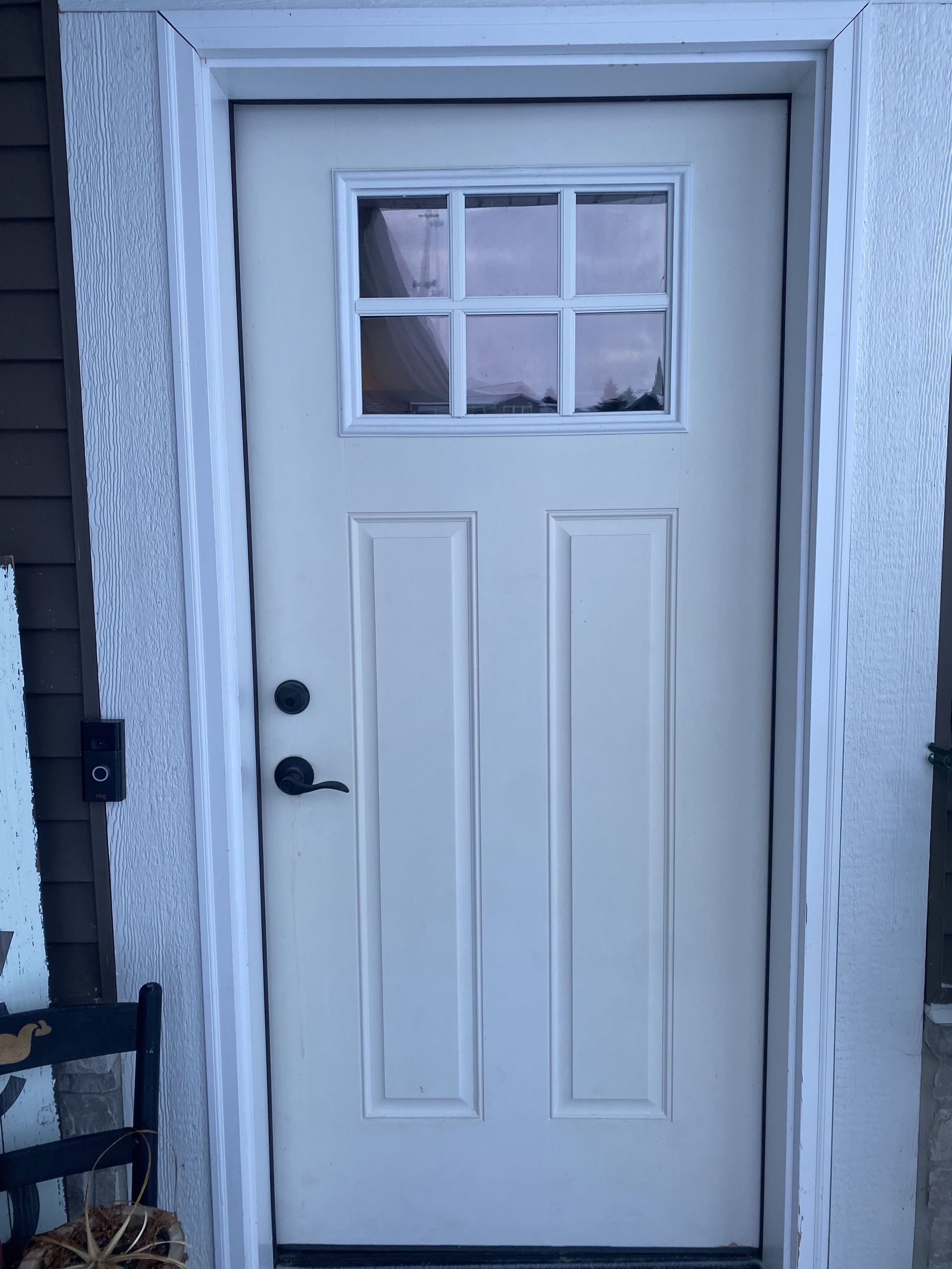 White front door with a small window and black handle, set in a snow-covered entryway.