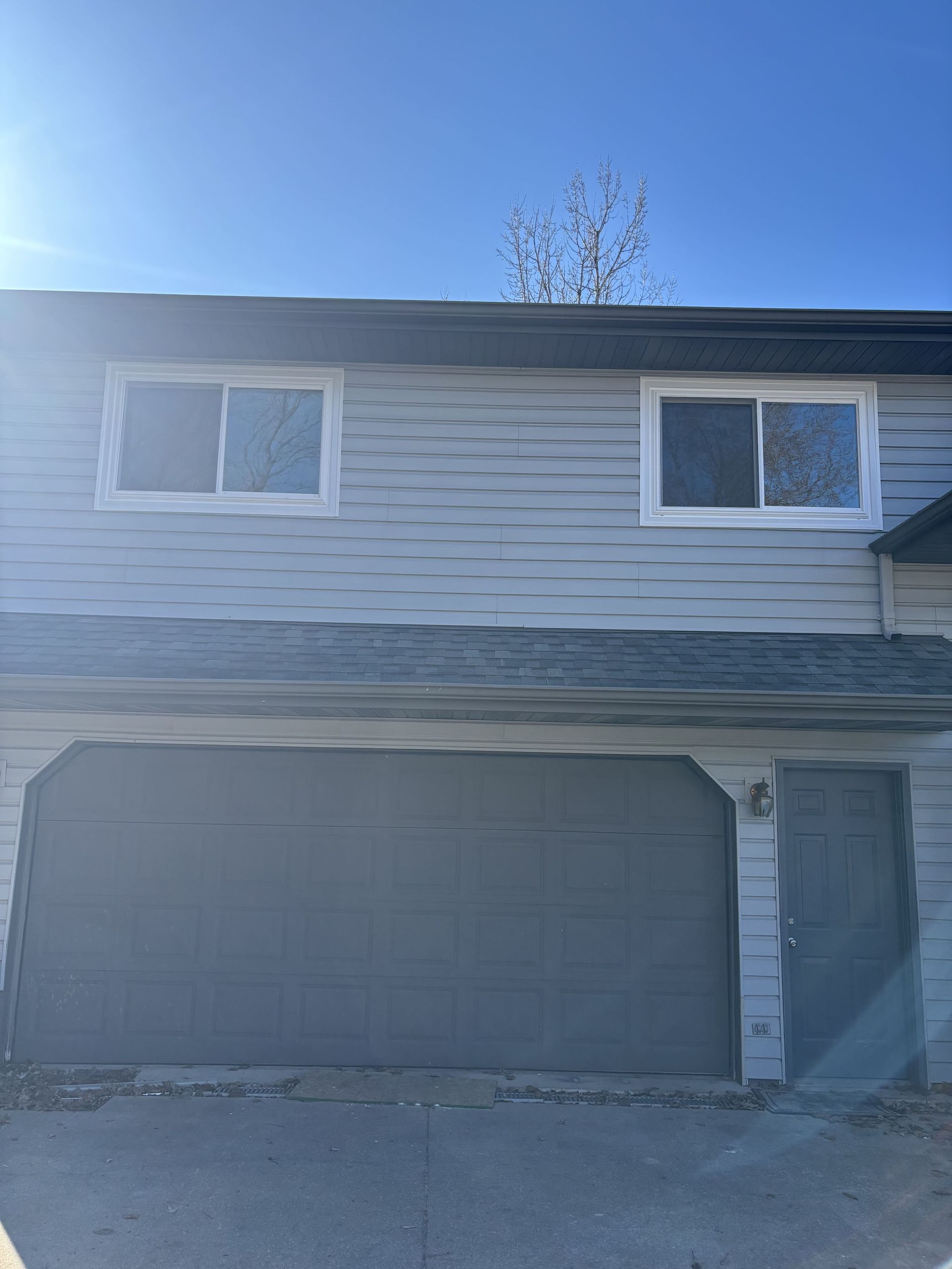Two-story house with gray garage door and siding, bright blue sky above