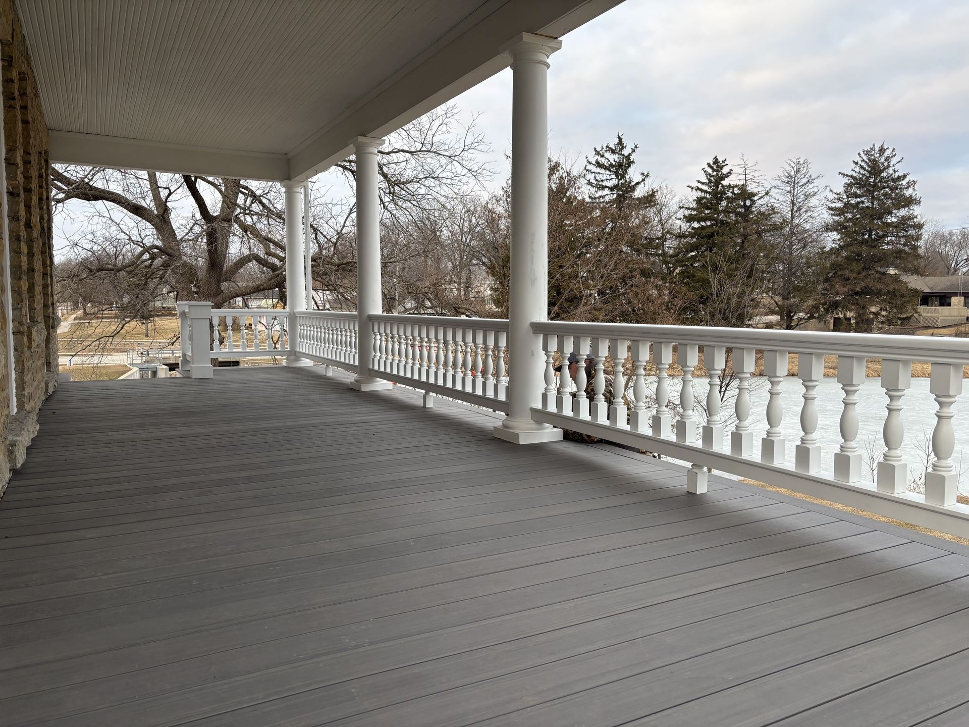 Covered front porch with gray floorboards, white railing and columns, overlooking a wintery yard.