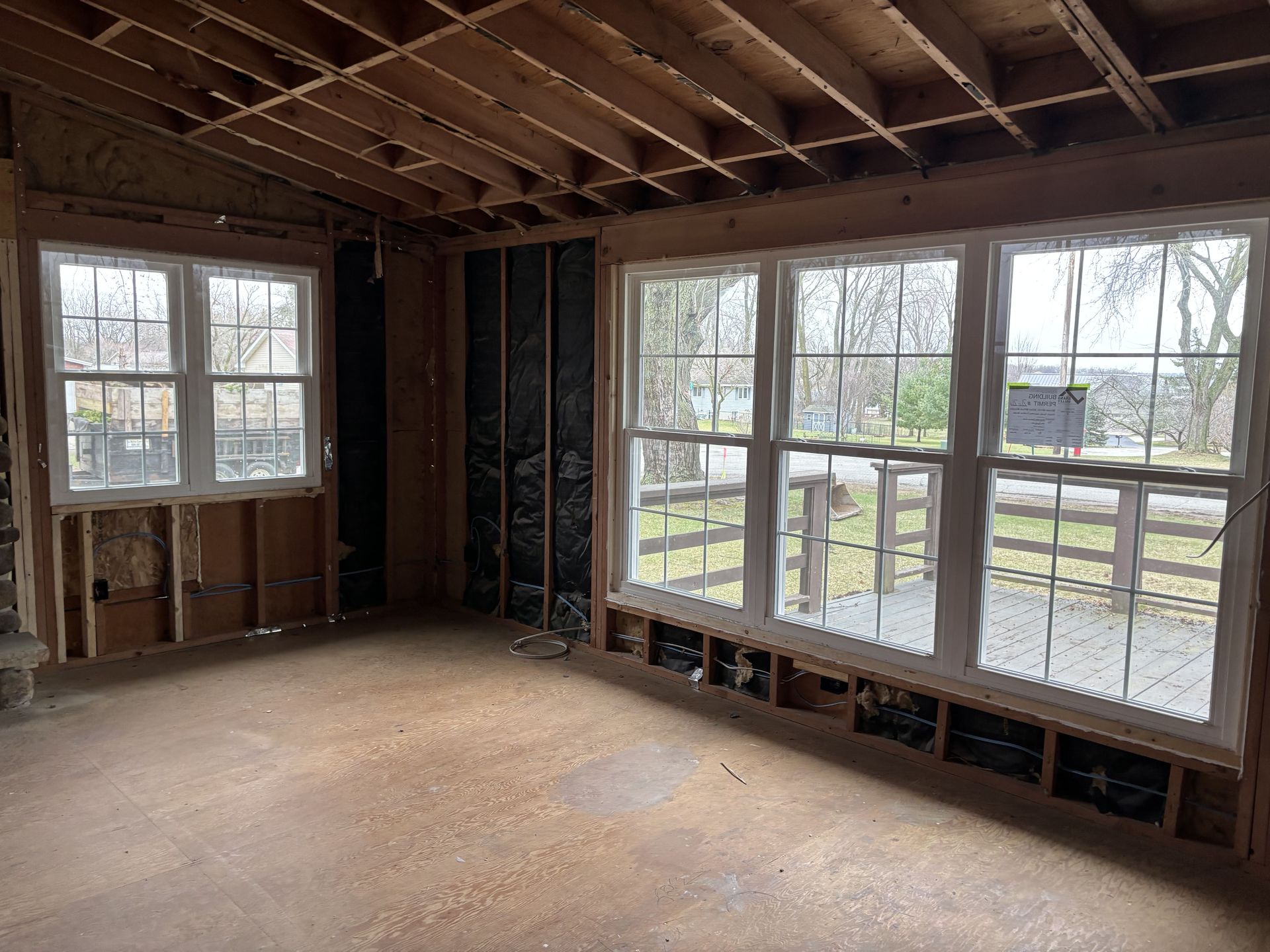 Unfinished room with exposed framing, large windows, and a view of a deck outside.