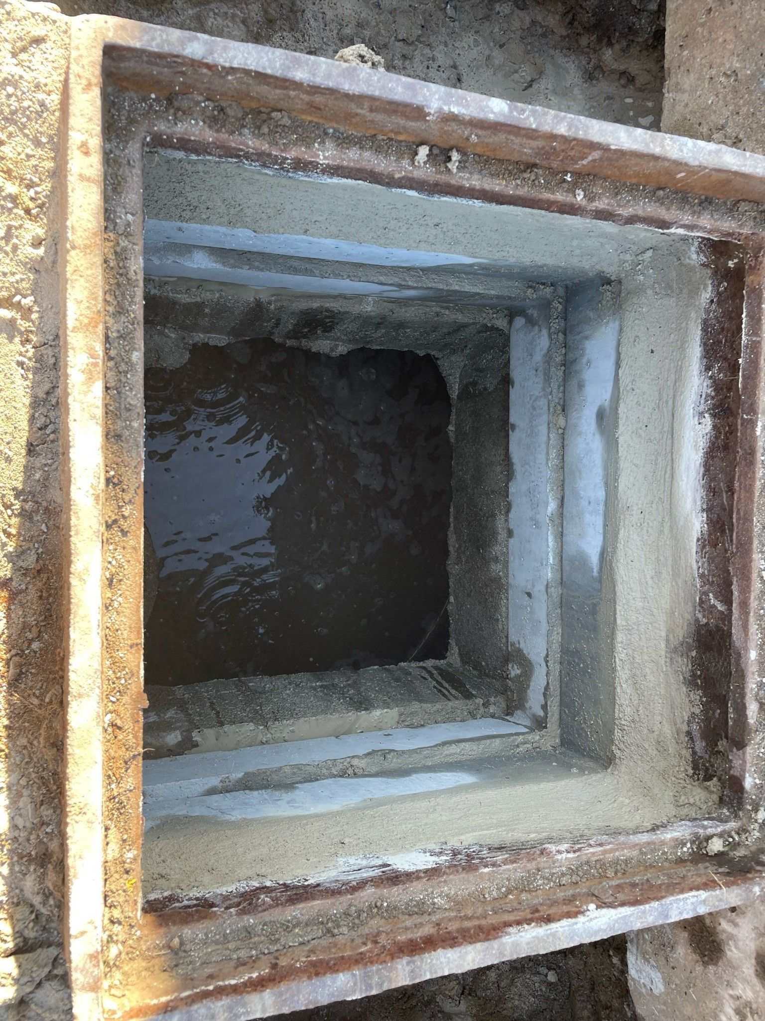 A square hole in the ground with a metal frame surrounding it.