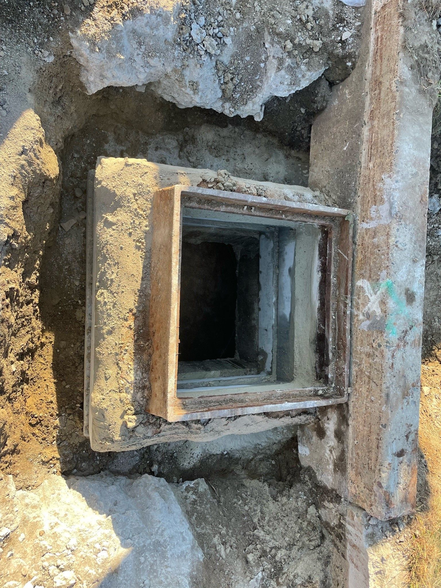 A square hole in the ground next to a concrete wall.