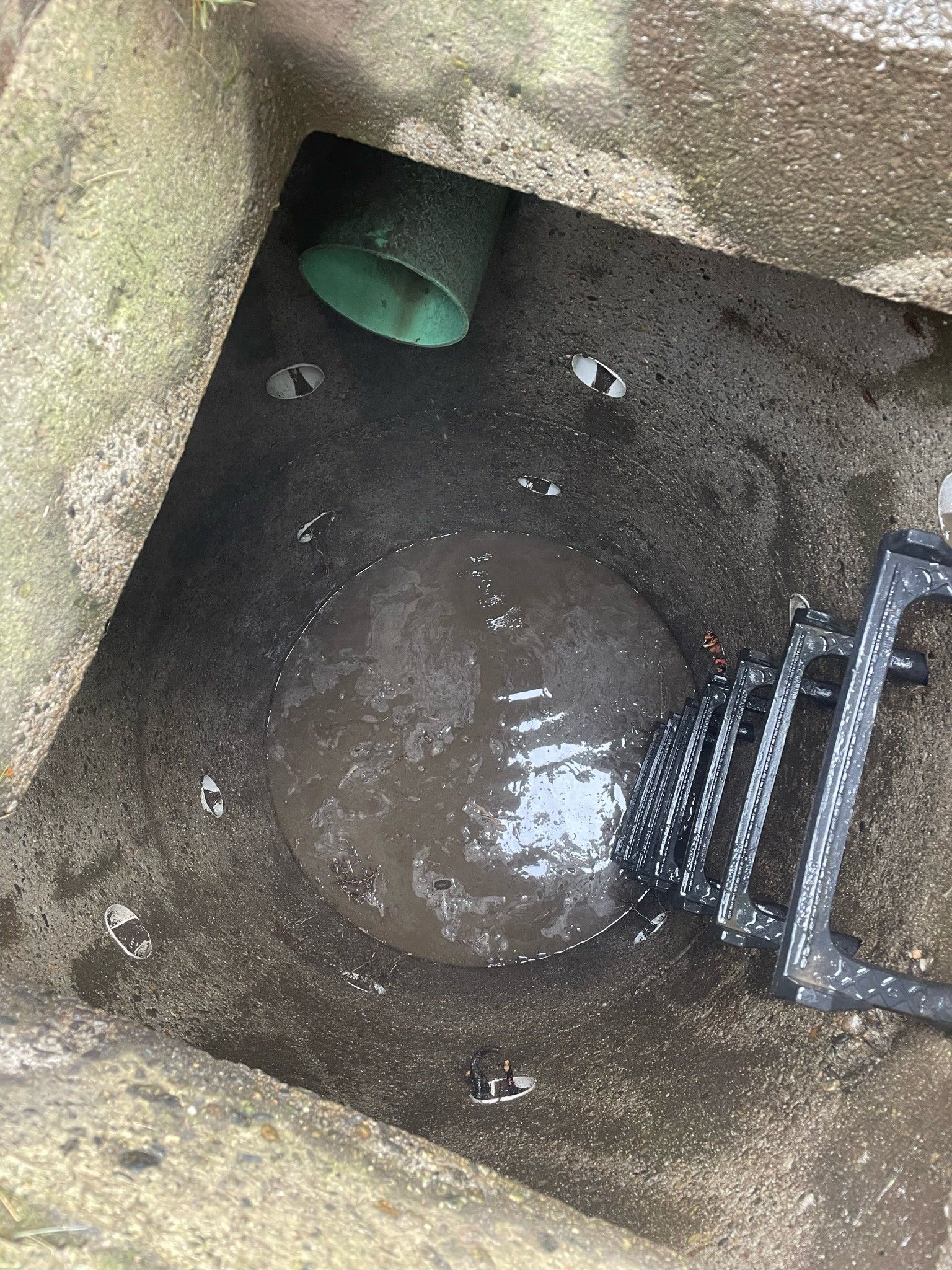 A manhole cover with a green pipe coming out of it.