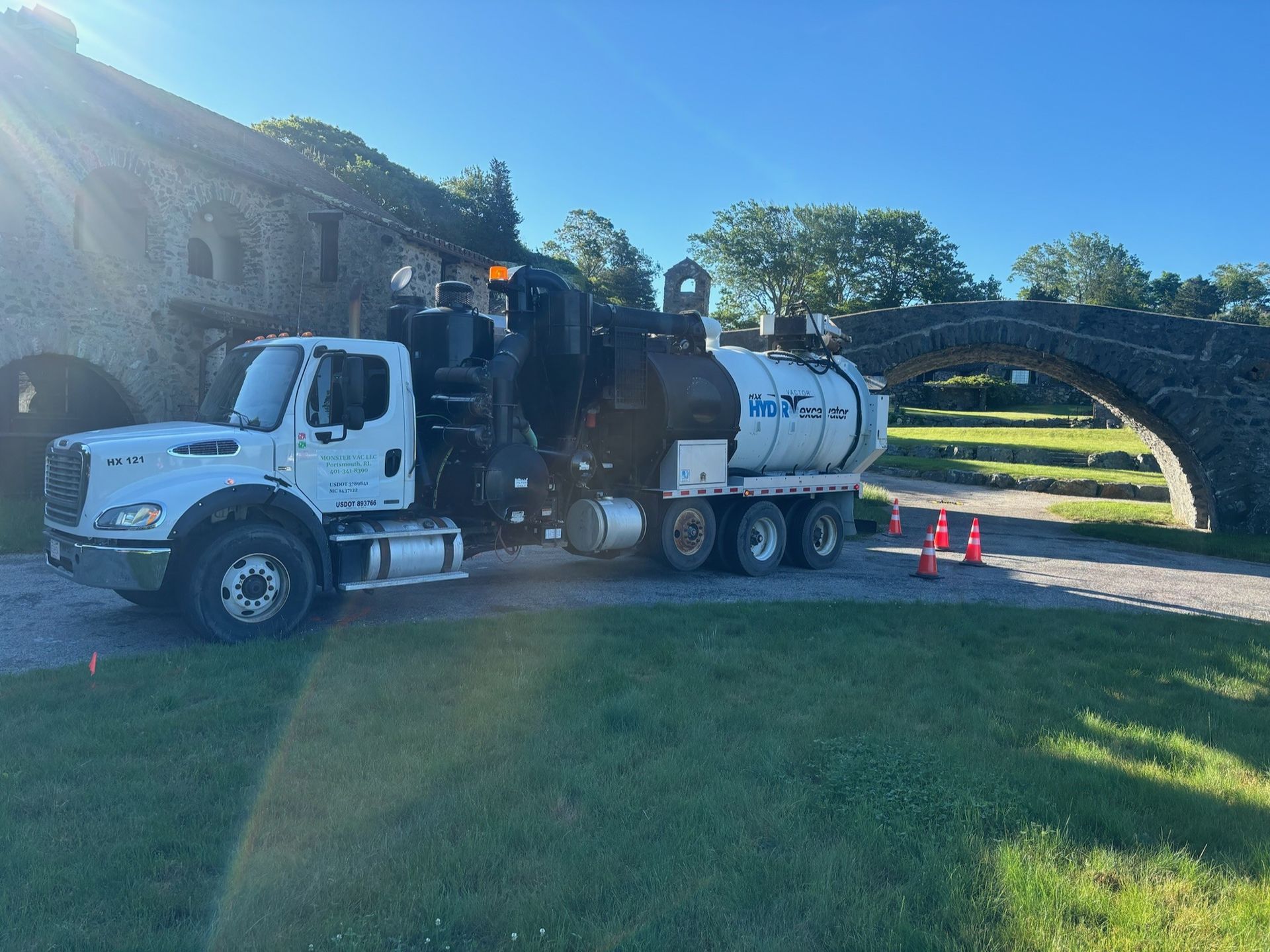 A vacuum truck is parked in front of a stone bridge.