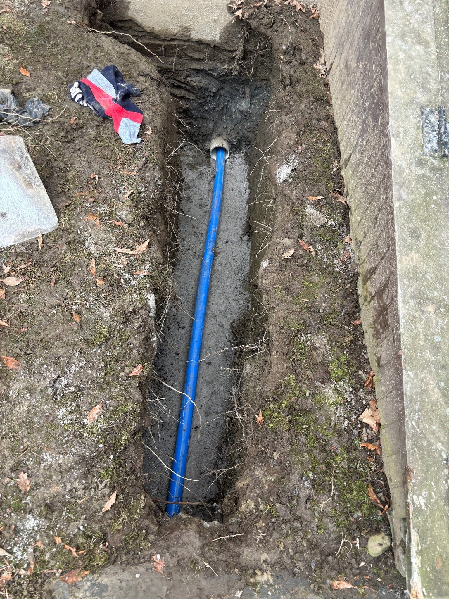 A blue pipe is laying in the dirt next to a shovel.