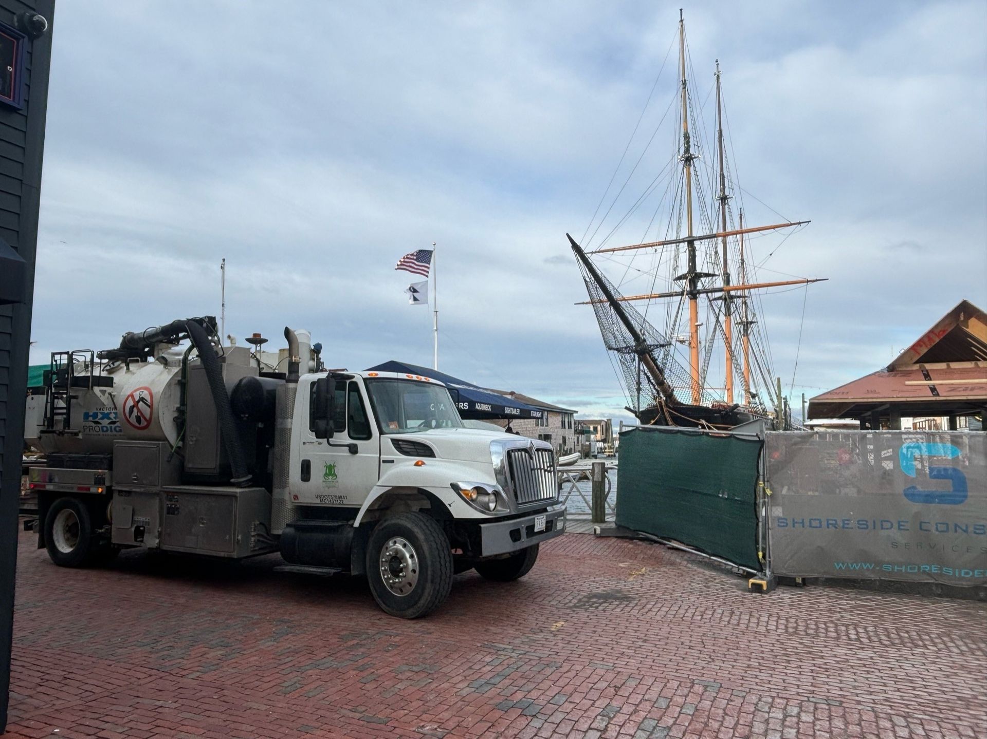 A vacuum truck is parked in front of a large sailboat.