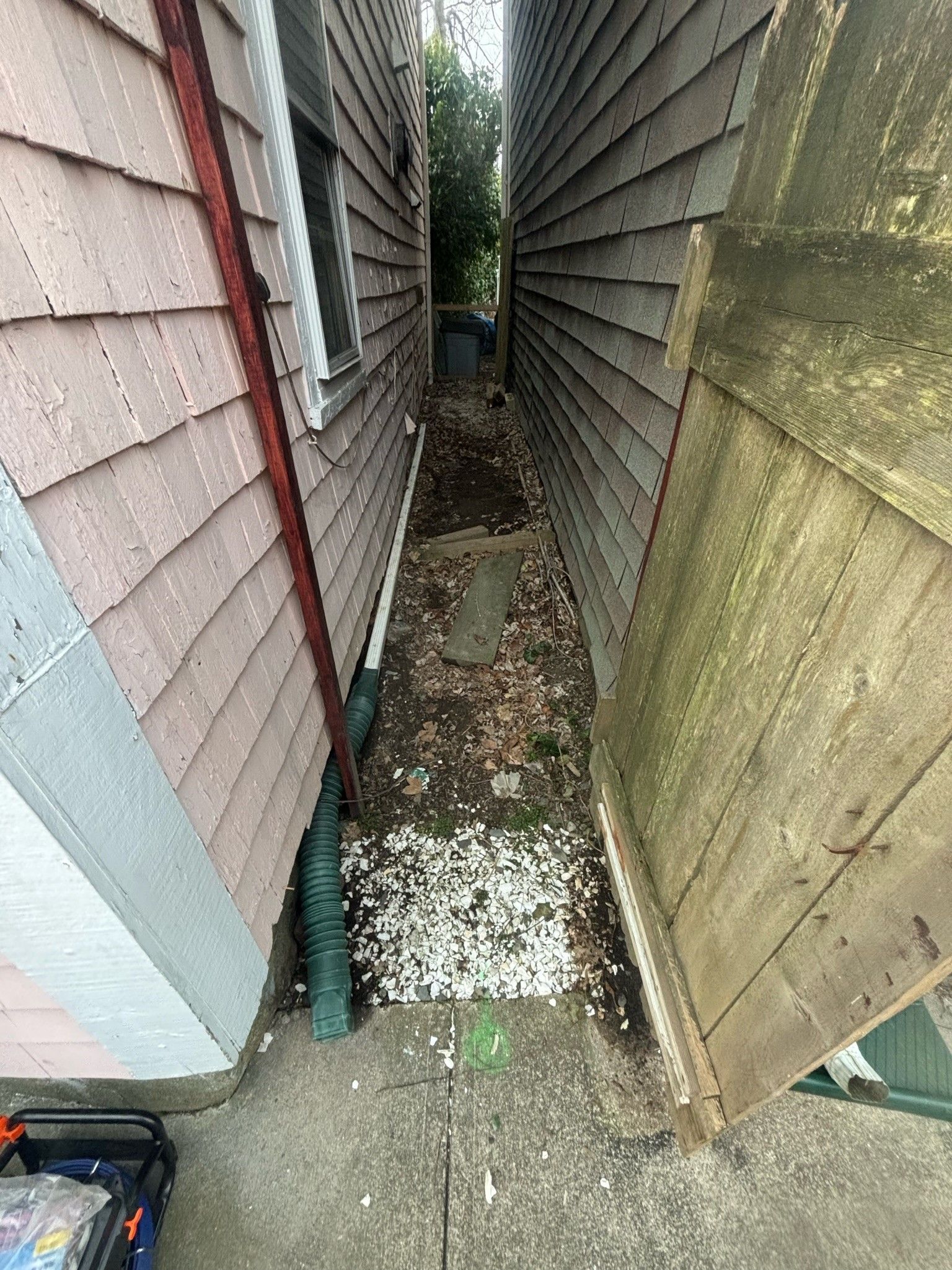 A narrow alleyway between two houses with a wooden fence.