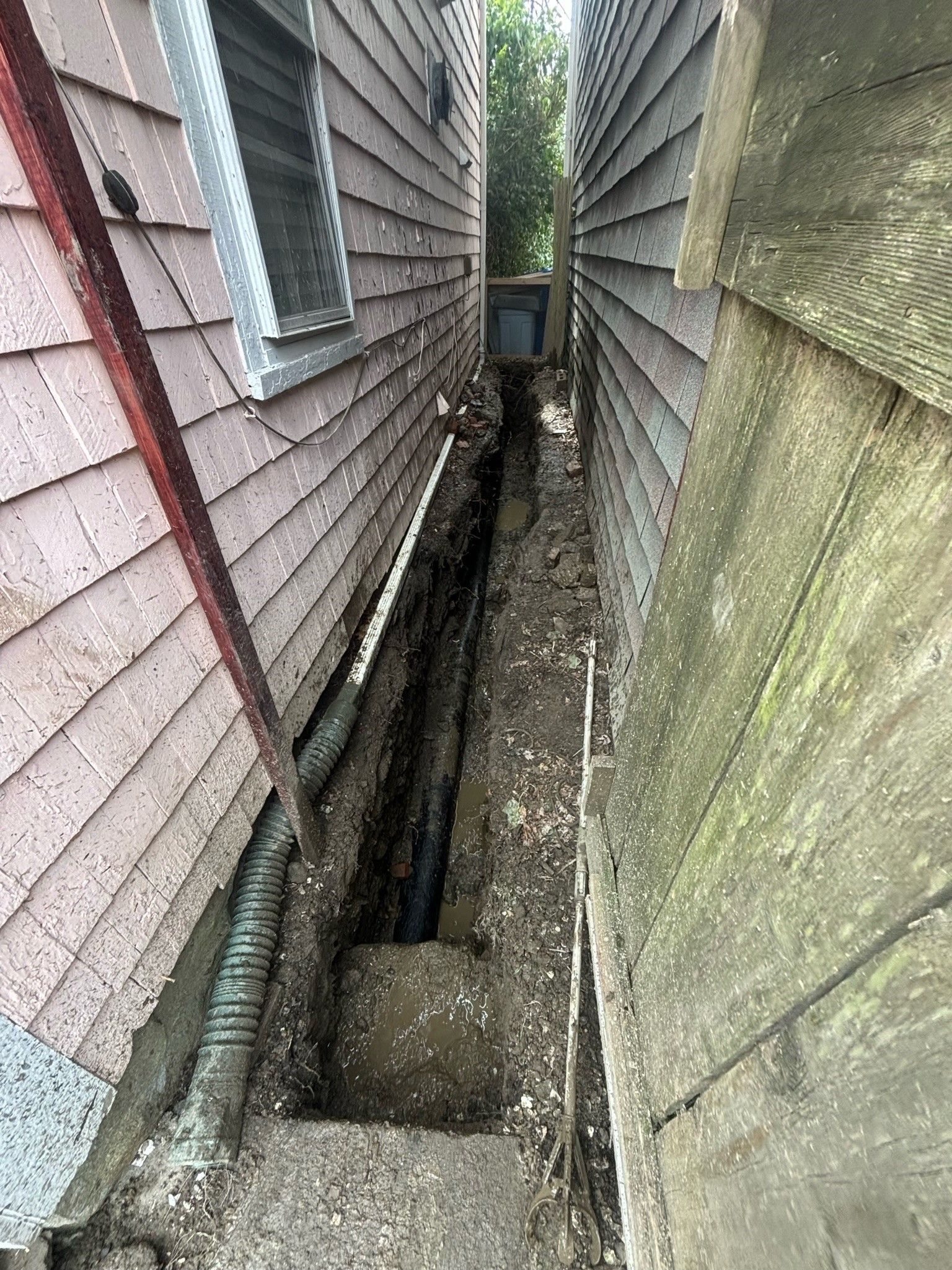 A narrow alleyway between two houses with a hole in the ground.