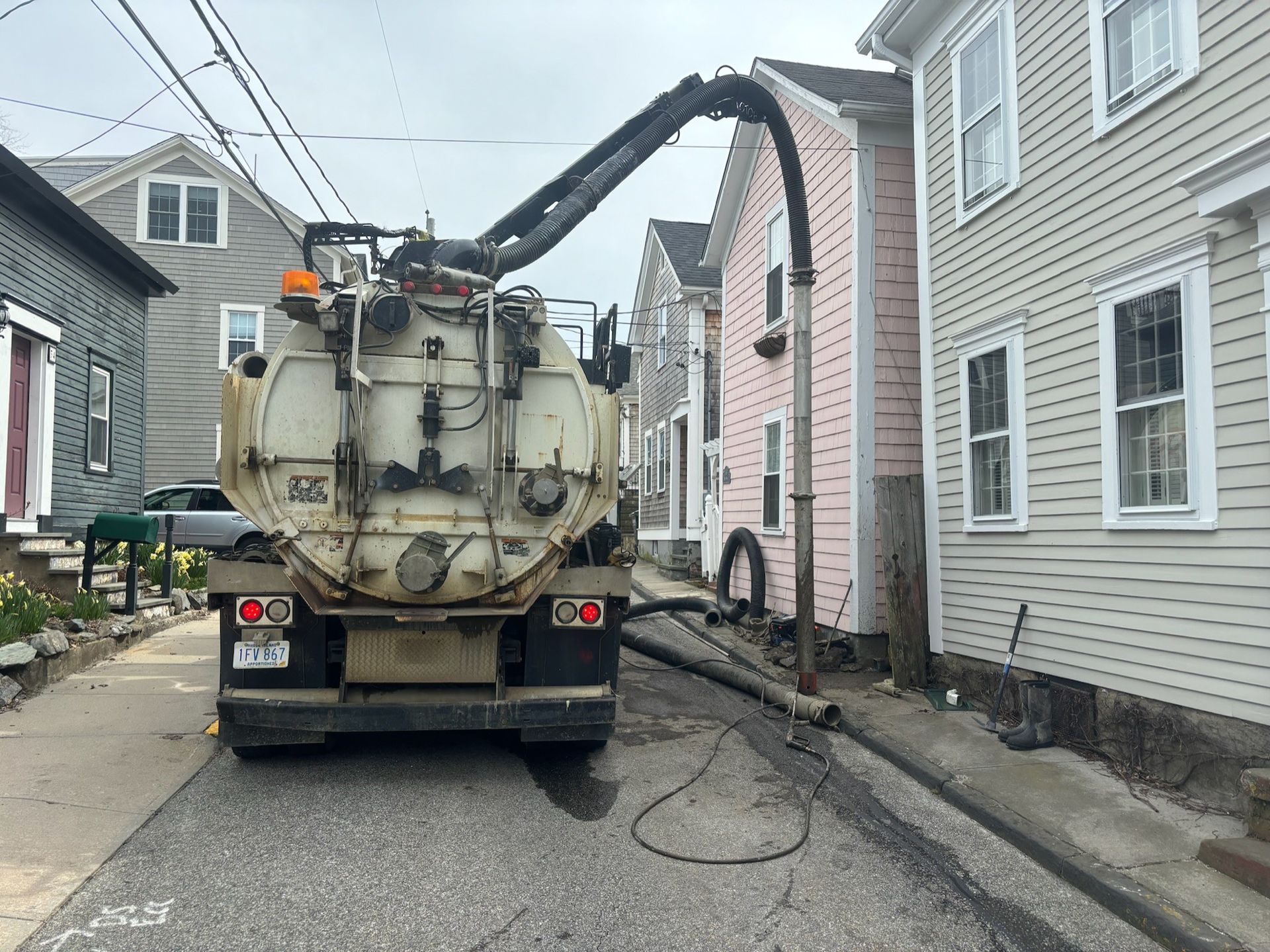 A vacuum truck is driving down a street between two houses.