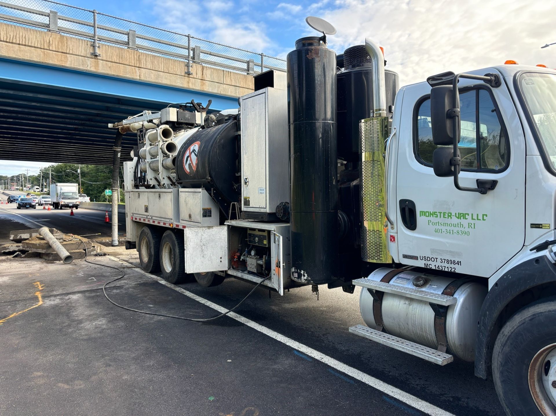 A vacuum truck is parked on the side of the road under a bridge.