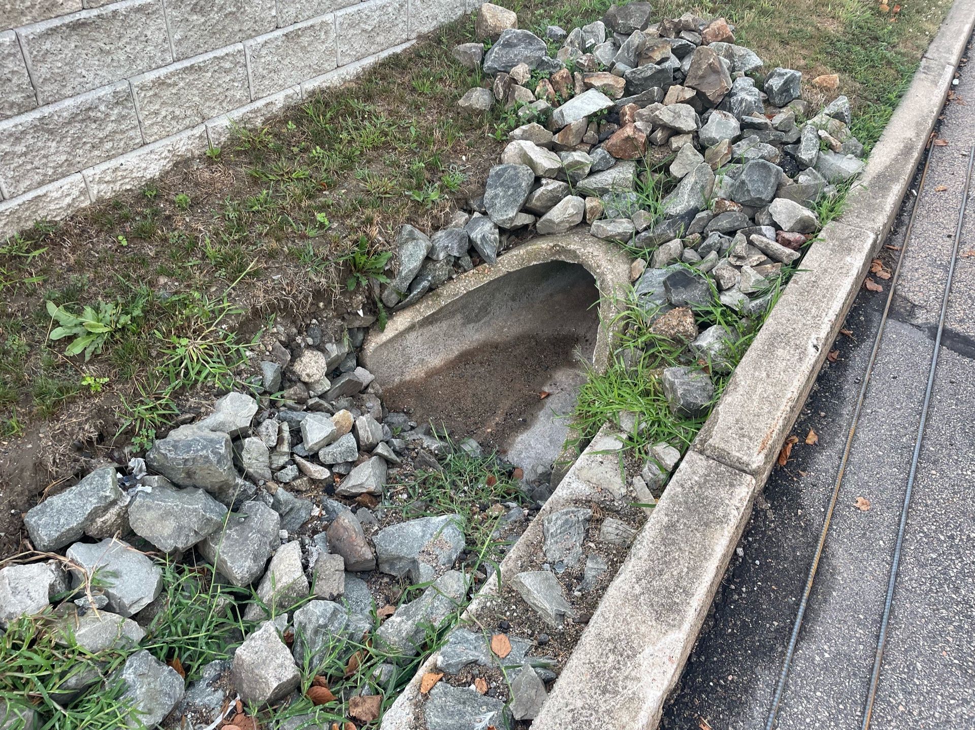 A drainage pipe is surrounded by rocks on the side of the road.