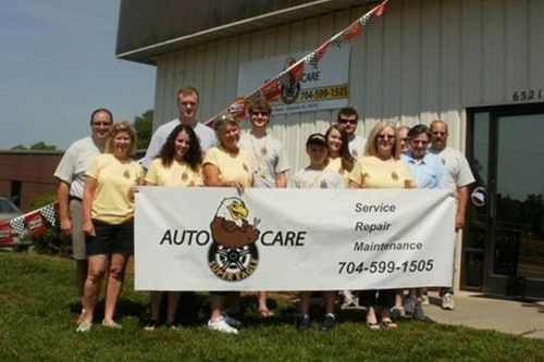 Group holding an Auto Care banner outside a shop decorated with red, white, and blue bunting.