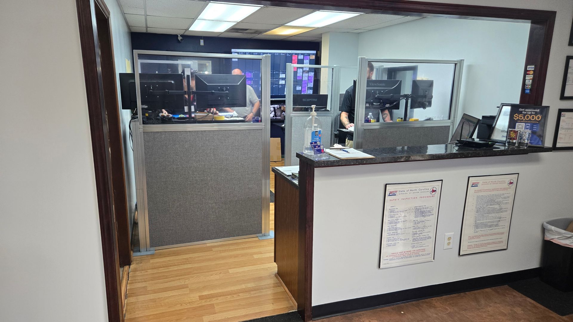 Reception desk with glass partition and counters in a lobby area, viewed through a doorway.