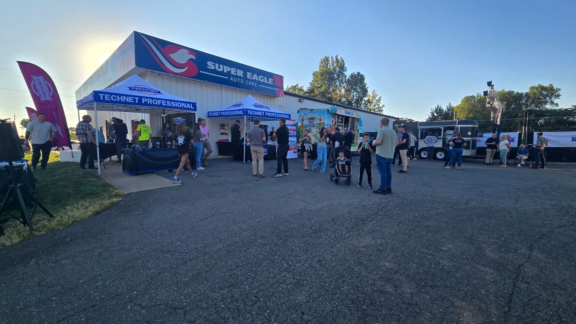 People gathered outside a blue-and-white event tent on a sunny day.
