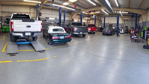 Auto repair shop with several cars on lifts and in service bays inside a large garage.