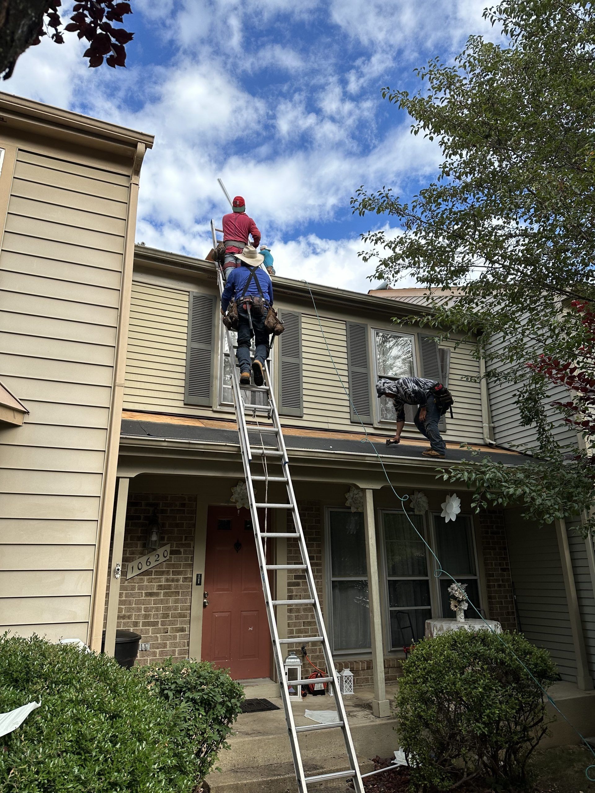 Workers on ladders repairing the roof and gutters of a two-story house.