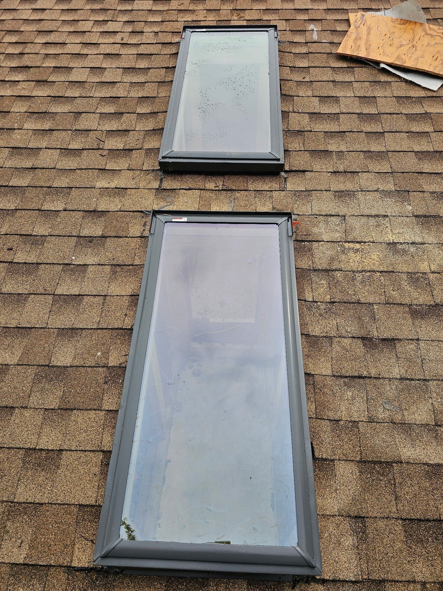 Two rectangular skylights on a shingled roof, one above the other.