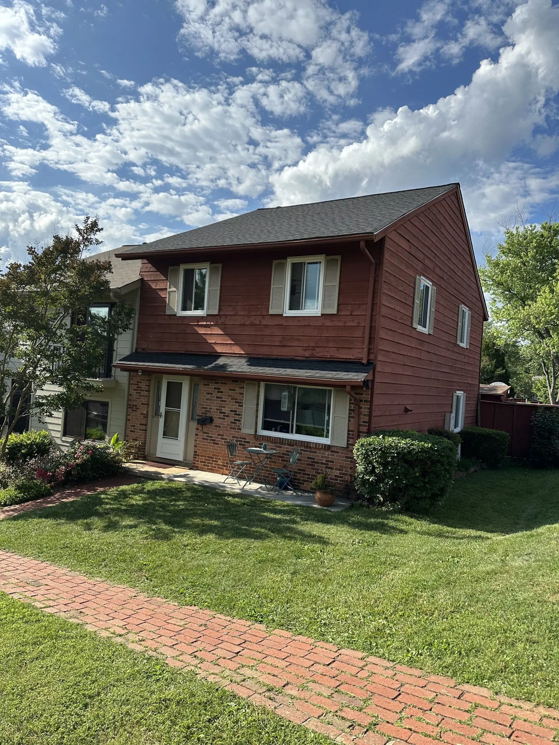 Two-story red brick house with a lawn and brick walkway under a partly cloudy sky
