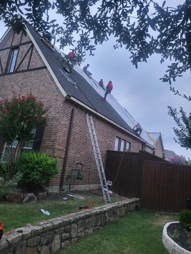 Brick house roof under repair with workers on top and a ladder against the wall