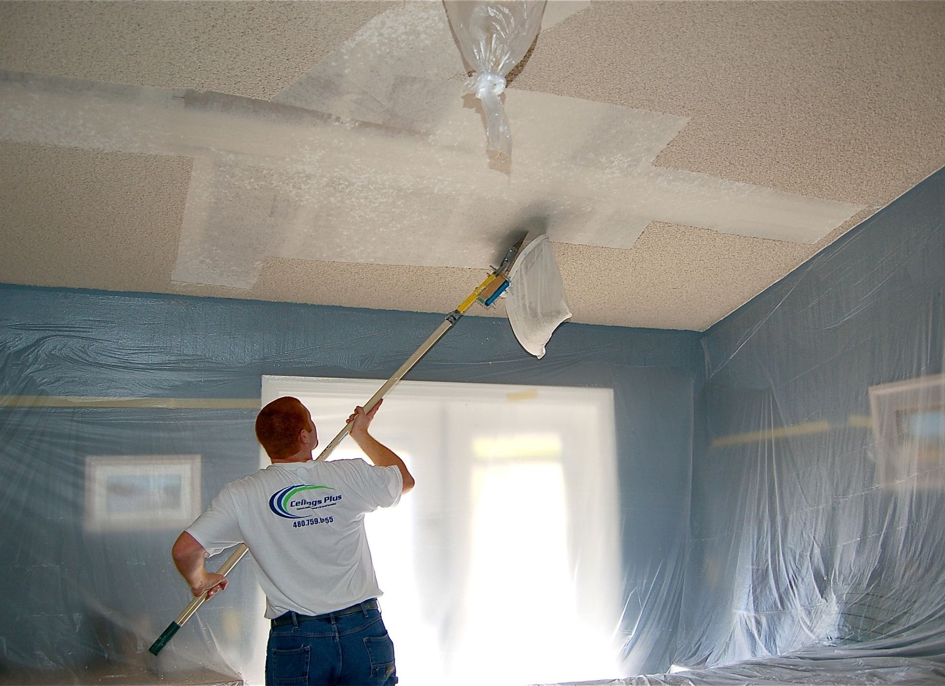 A man is painting the ceiling of a room with a roller