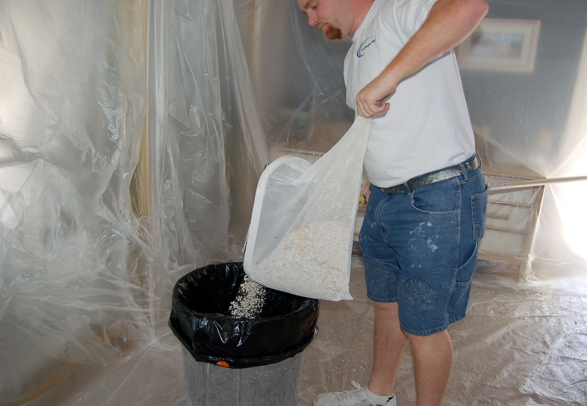 A man is pouring a bag of white powder into a trash can.