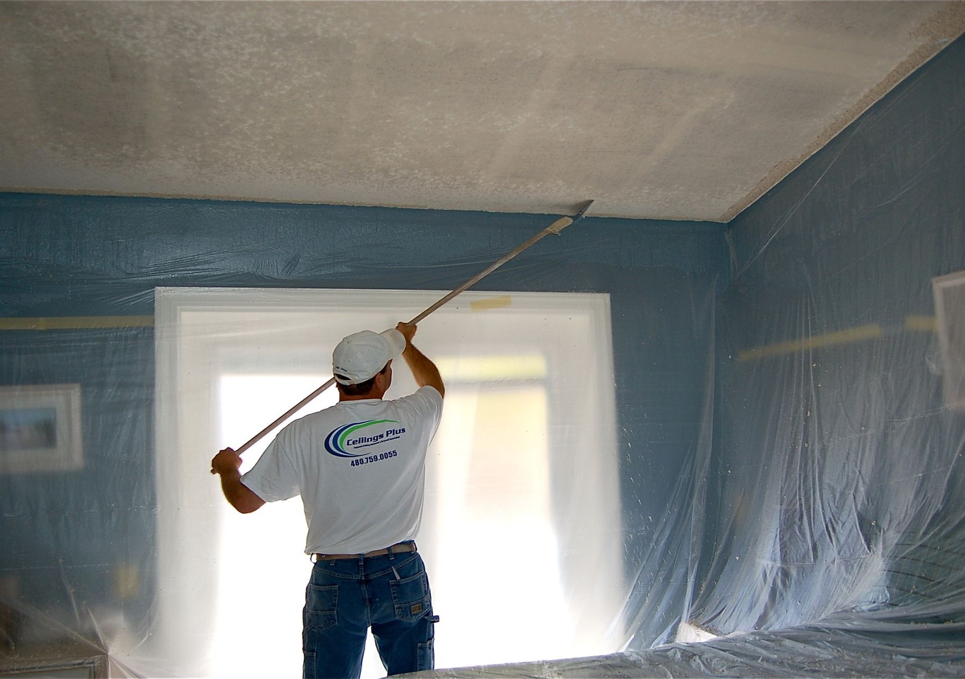A man is painting the ceiling of a room with a roller.