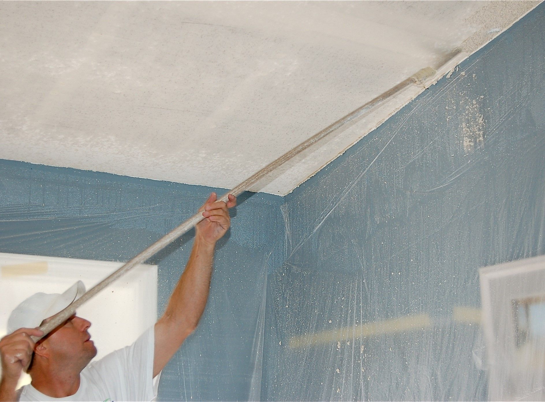 A man is painting the ceiling with a paint roller