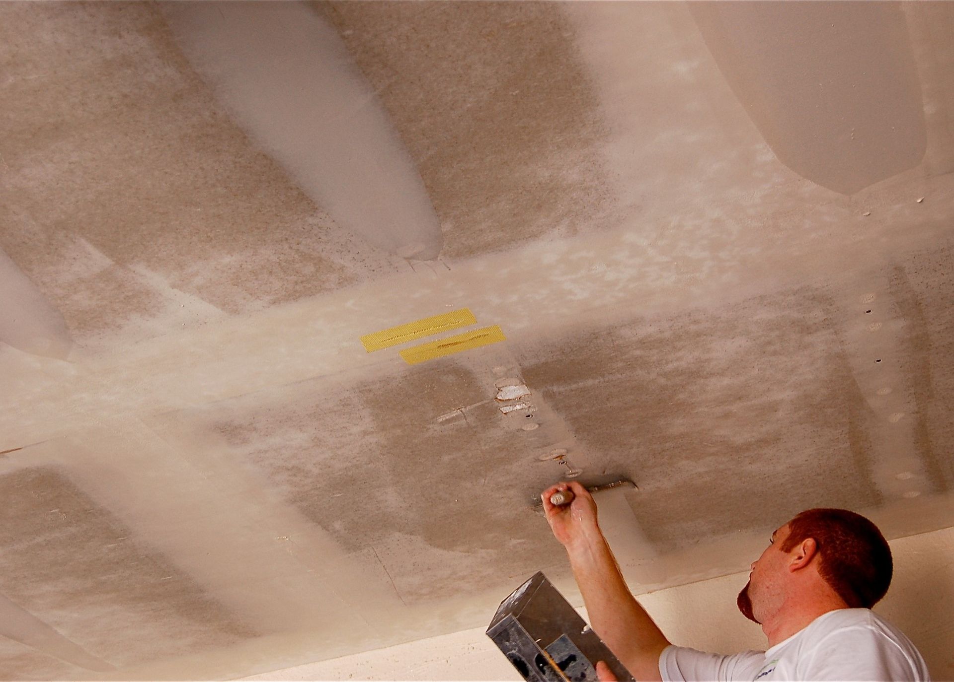 A man is painting a ceiling with a spatula.