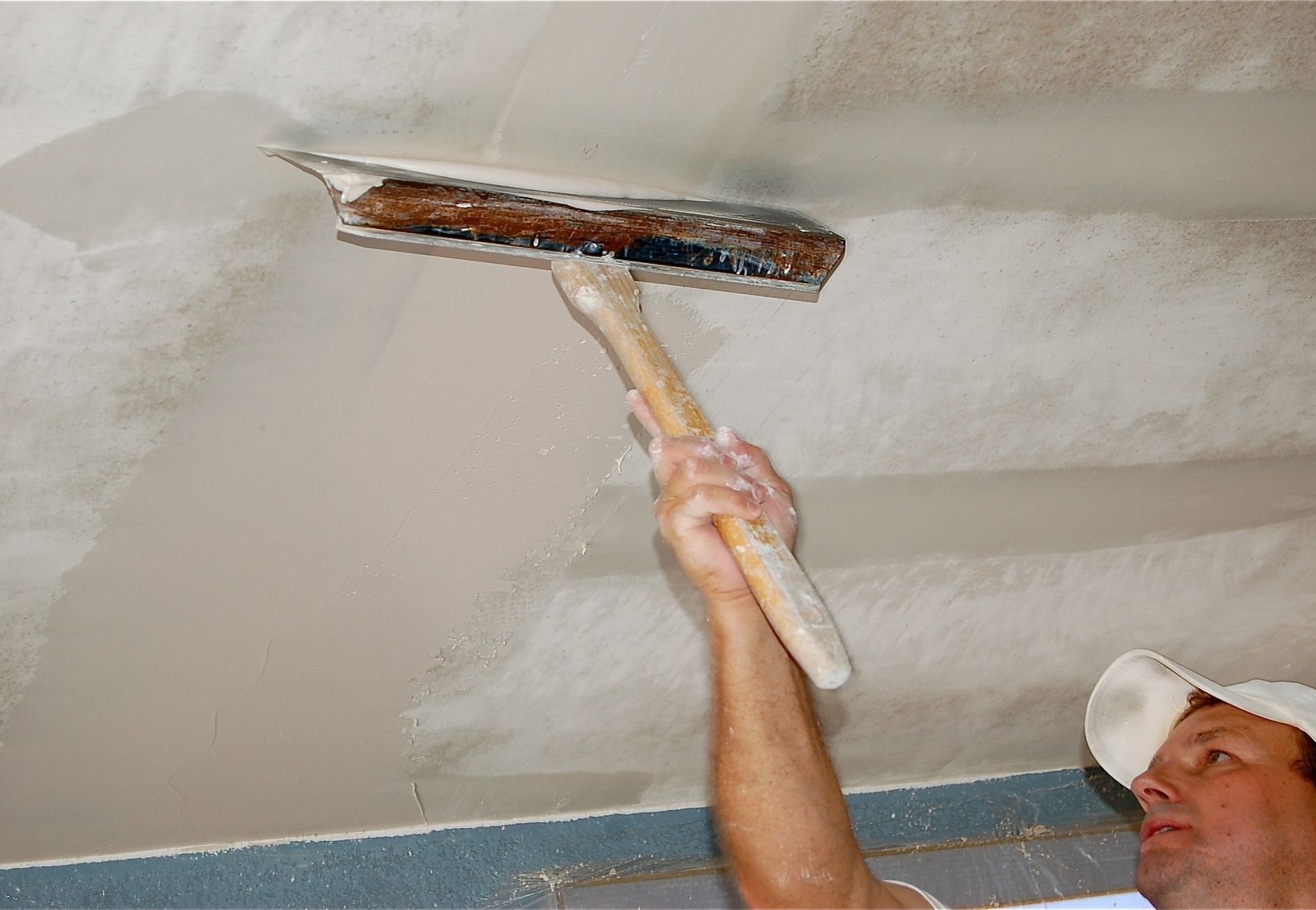 A man is plastering a ceiling with a trowel.