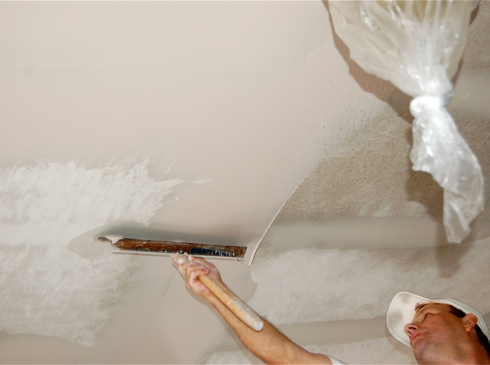A man is plastering a ceiling with a trowel.